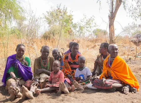 Grupo de habitantes de uma vila africana sentados no chão, olhando para a câmera.