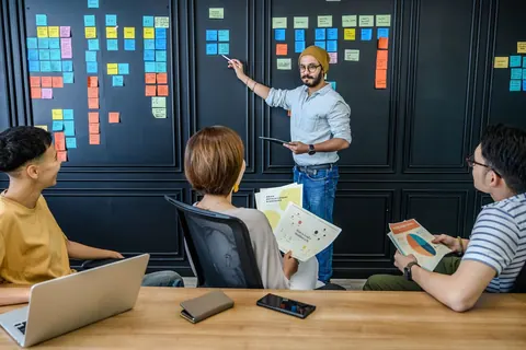 Equipe de RH em reunião, homem apontando para post-its em um quadro.