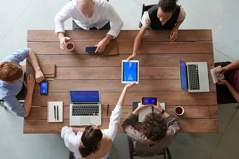 Pessoas em uma mesa de reunião com laptops e tablets, discutindo e colaborando.