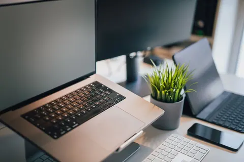Laptop em um escritório moderno com monitor e planta, simbolizando tecnologia e trabalho.