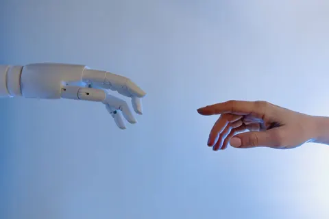 Mão robótica e mão humana se aproximando sobre fundo azul