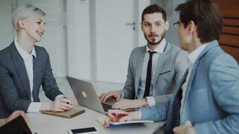 Profissionais em reunião de negócios, com laptop e anotações na mesa.