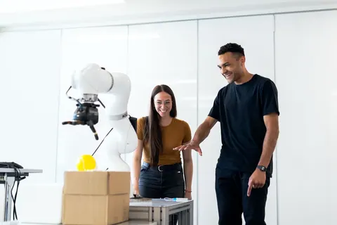Engenheiros sorrindo enquanto trabalham com um braço robótico em um laboratório.